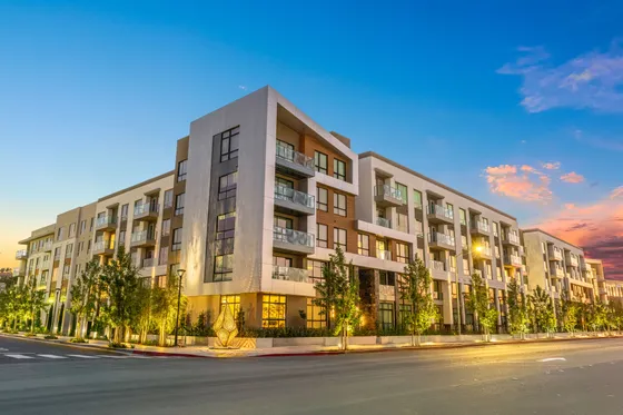 Modern apartment building with large windows and private balconies, set against a stunning sunset backdrop; ideal for contemporary urban living.
