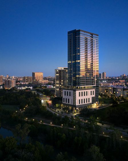 Elegant high-rise apartment building at twilight, towering over a vibrant cityscape with lush greenery, reflecting the golden hues of the setting sun.