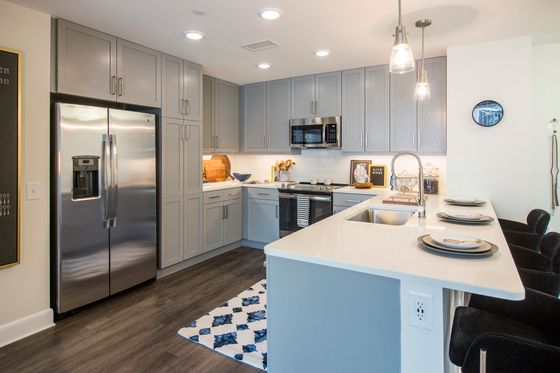 Elegant kitchen featuring sleek stainless steel appliances, stylish gray cabinetry, and a spacious white quartz island with modern pendant lighting.
