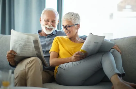 Man Woman Couple Happy Reading Newspaper on Couch Smiling Laughing