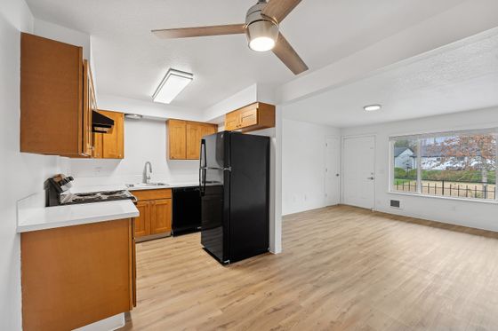 Bright open kitchen with wooden cabinets, sleek black appliances, and attached living area with large window.