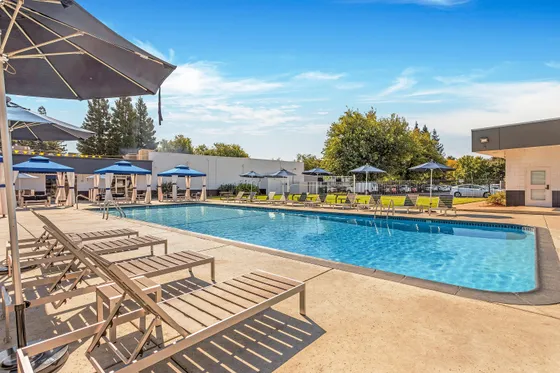 Inviting pool area with lounge chairs and umbrellas at a modern apartment complex.