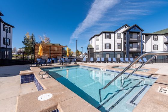 Inviting outdoor pool area with modern loungers and vibrant umbrellas, set against stylish apartment buildings.