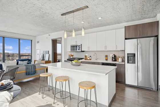 Sleek modern kitchen with spacious island, stainless steel appliances, and bright open living area with large windows offering stunning views.