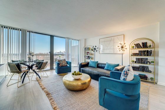 Chic living room with elegant blue seating, a stylish gold coffee table, and modern decor, featuring stunning city views through expansive windows.