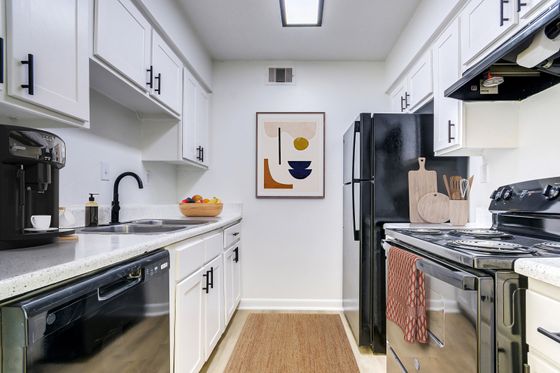 Modern kitchen with sleek black appliances, bright white cabinetry, and stylish decor. Features an espresso machine, artful wall piece, and inviting layout.