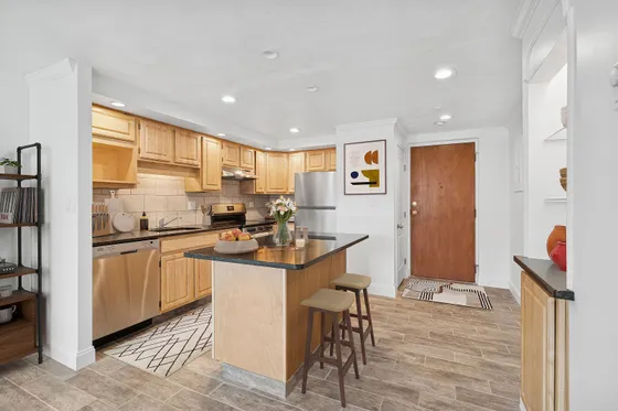 Modern kitchen with stainless steel appliances, inviting island, and chic wooden cabinetry in elegant apartment setting.