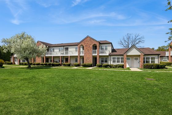 Charming brick apartment complex with beautiful landscaping and vibrant green lawns, set under a bright blue sky.