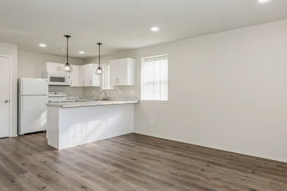 Modern kitchen with elegant white cabinetry, marble countertops, and stylish pendant lighting, complemented by sleek hardwood flooring for a contemporary living space.