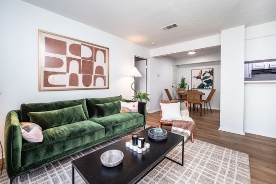 Chic living room with a plush green sofa, abstract art, and seamless flow into a stylish dining area.
