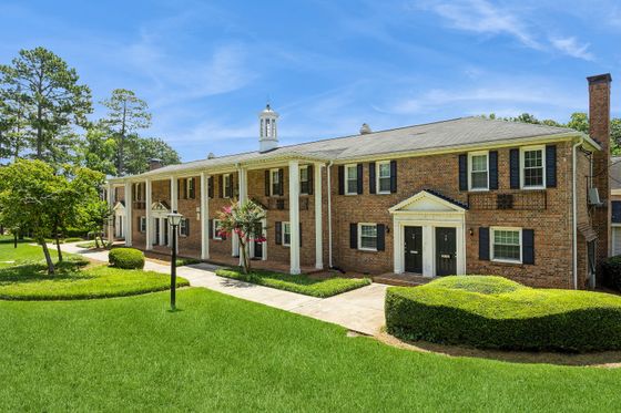 Charming brick apartment building with classic architectural style, nestled in lush greenery under a vibrant blue sky.