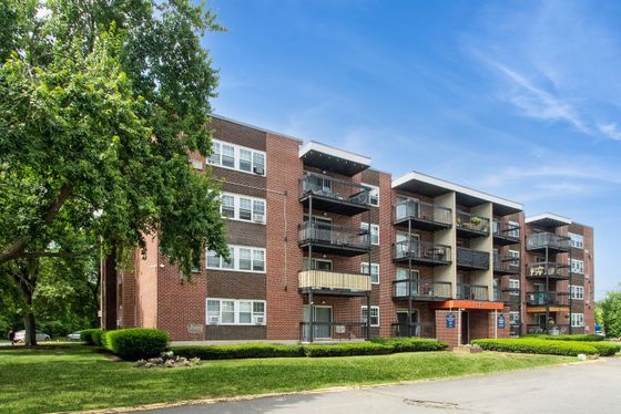 Charming brick apartment building with balconies, surrounded by lush greenery and a bright blue sky, offering a serene living environment.
