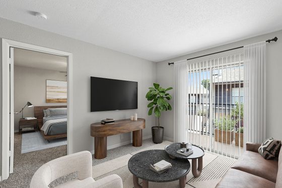 Inviting living room with modern decor, natural light streaming through large sliding doors, leading to a cozy bedroom.