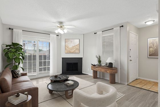 Elegant living room featuring a cozy brown leather sofa, stylish round coffee tables, and a fireplace. Bright natural light fills the room through large windows with white curtains, complemented by a lush green plant for a welcoming touch.
