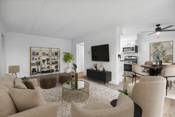 Modern open-concept living space featuring a chic beige sofa, elegant round coffee table, and stylish dining area leading to a sleek kitchen with stainless steel appliances.
