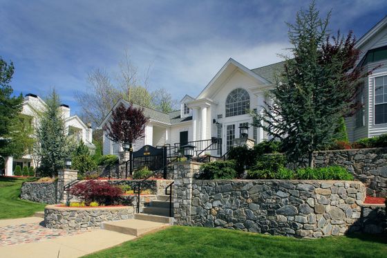 Charming suburban home with classic white siding, elegant columns, and lush landscaping, offering a welcoming and picturesque entrance.