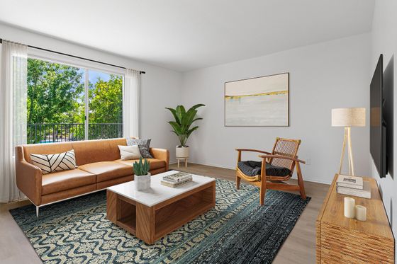 Chic, sunlit living room with modern decor, featuring a sleek leather sofa, elegant wooden accents, and a large window overlooking lush greenery.