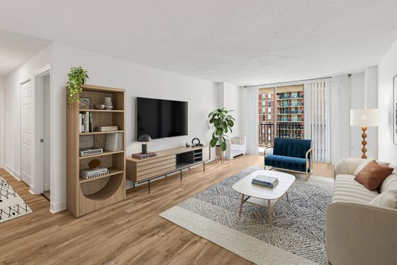 Bright and airy living room with modern furnishings, featuring a plush navy chair, stylish sofa, and decorative bookshelf, complemented by a large flat-screen TV and floor-to-ceiling windows revealing a cityscape view.