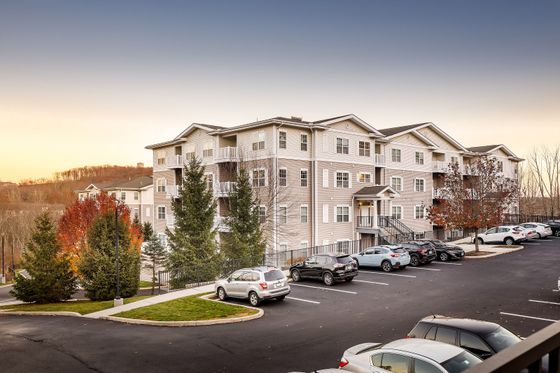 Charming apartment complex at sunset, surrounded by lush trees and modern parking facilities, offering serene living amidst nature.