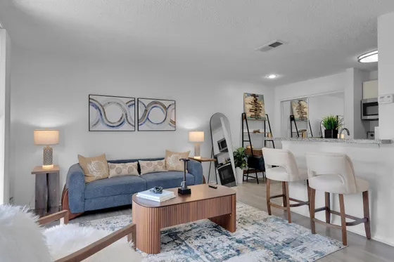 Chic living room with stylish blue sofa, modern art, and sleek open-concept design featuring a cozy kitchen bar area.