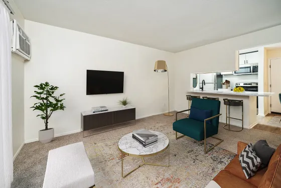 Chic modern living room with elegant decor featuring a cozy seating area, large wall-mounted TV, stylish coffee table, and a view into a sleek open-concept kitchen with breakfast bar.