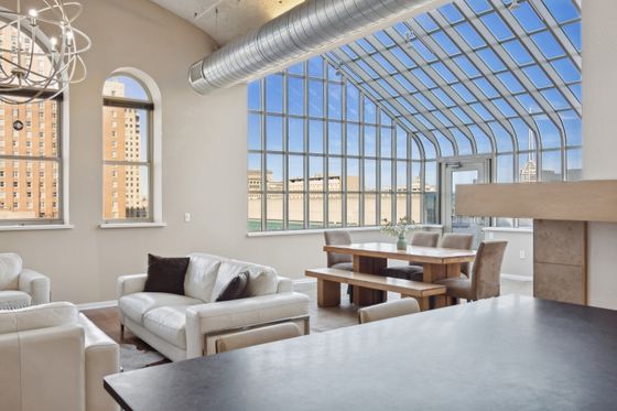 Bright and spacious apartment with modern leather sofas, a stylish dining area, and expansive city views through large, arched windows.