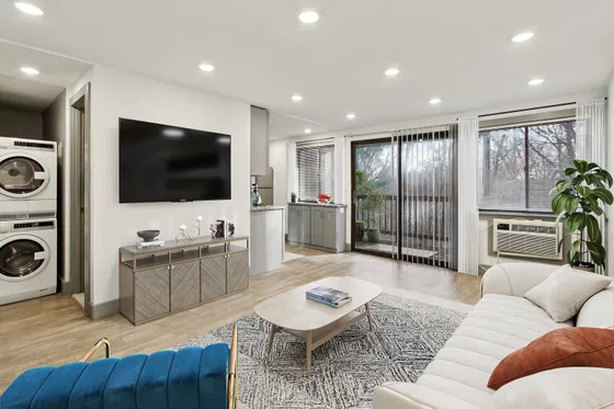 Modern living room with plush seating, elegant decor, wall-mounted TV, and floor-to-ceiling windows offering scenic views. Includes in-unit washer and dryer for convenience.