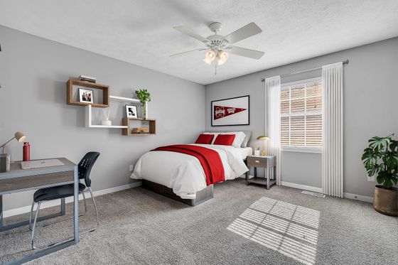 Inviting bedroom with gray walls, contemporary bookshelf, and a cozy bed adorned with red accents, illuminated by natural light through a large window.