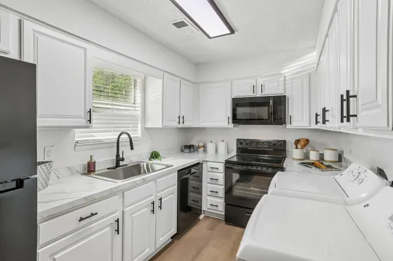 Bright and modern kitchen with sleek white cabinetry, elegant marble countertops, and top-notch black appliances.
