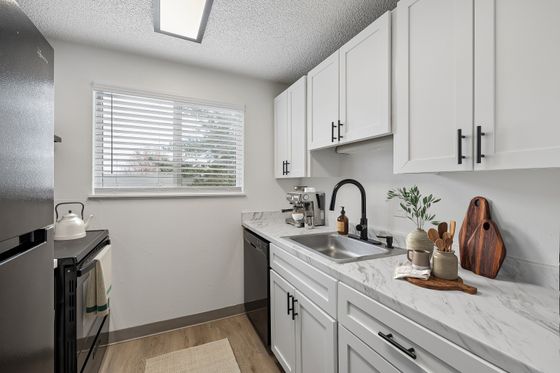 Modern kitchen with sleek white cabinets, elegant marble countertops, and natural light streaming in through a large window.