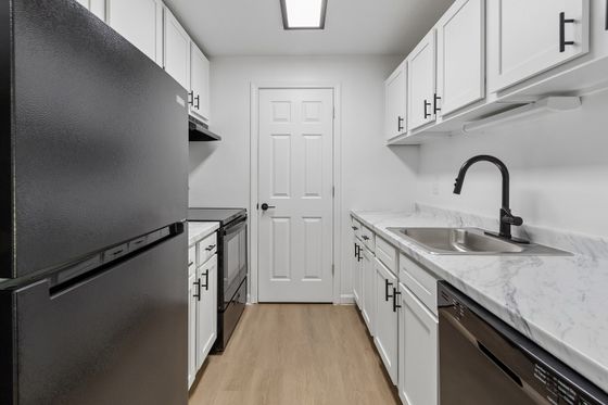 Sleek modern kitchen with stylish black appliances, elegant white cabinetry, and marble countertops.