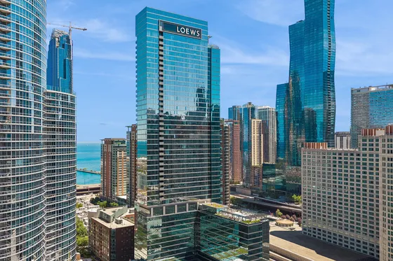 Stunning urban skyline view featuring modern high-rise buildings with reflective glass facades, set against a clear blue sky with glimpses of the lake in the background.