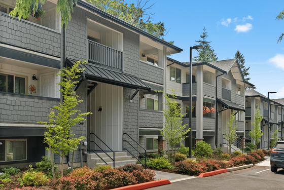 Charming apartment complex with modern gray siding, lush landscaping, and spacious balconies.
