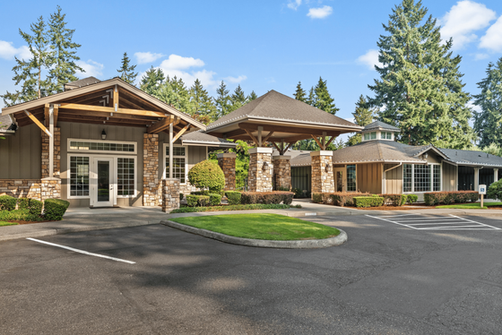 Inviting apartment complex exterior with charming stone and wood accents, surrounded by lush greenery and tall trees.