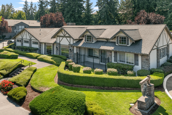 Charming Tudor-style house with lush landscaped gardens, gabled roof, and picturesque front porch, nestled in a tranquil green setting.
