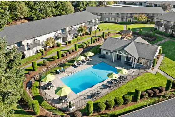 Aerial view of a modern apartment complex featuring a sparkling blue swimming pool, surrounded by lush green lawns and well-manicured landscaping, providing a serene and inviting atmosphere.