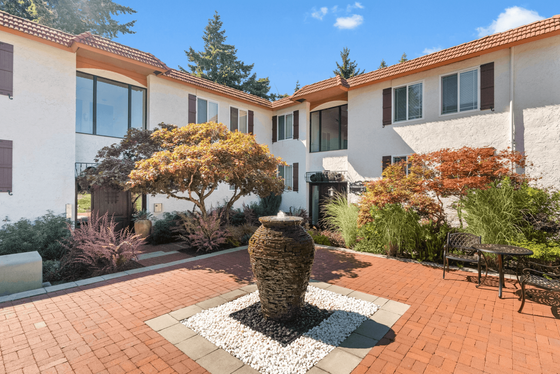 Charming apartment courtyard with lush greenery, elegant stone fountain, and a welcoming ambiance under a clear blue sky.