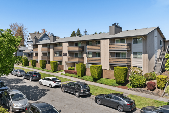 Charming three-story apartment building with spacious balconies, surrounded by lush greenery and ample street parking.