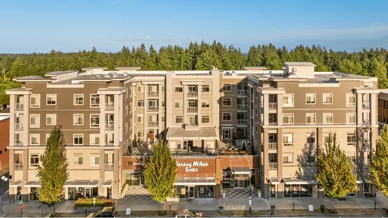 Elegant urban apartment complex with modern facade, surrounded by lush greenery and featuring ground-floor retail spaces.