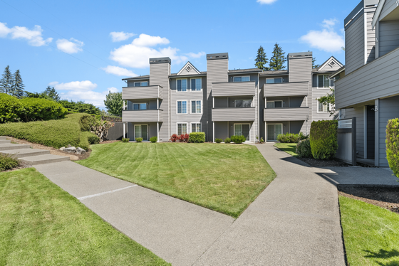 Charming apartment complex with modern architecture, featuring beautifully landscaped walkways and lush greenery under a bright blue sky.