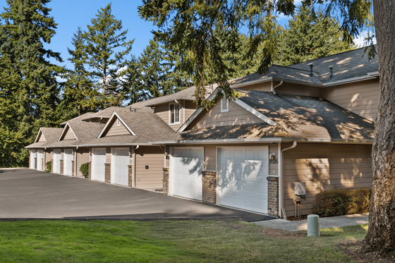 Charming row of modern townhouses with attached garages nestled among lush trees, offering serene suburban living.