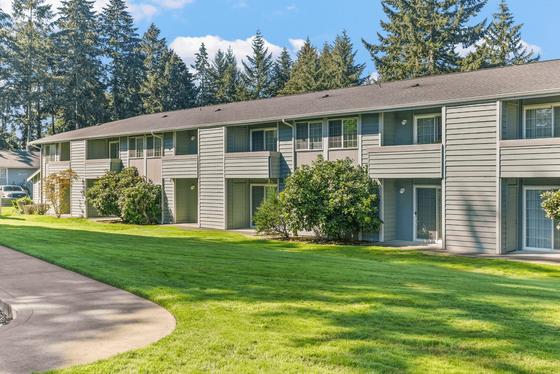 Charming two-story apartment complex nestled in a lush green landscape, featuring modern design and spacious balconies.