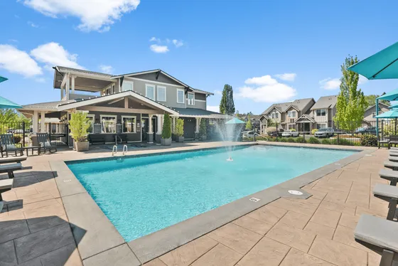 Inviting apartment complex with a sparkling pool, stylish seating, and lush greenery under a bright blue sky.