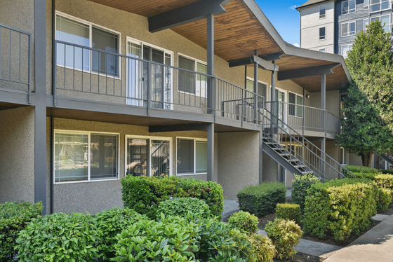 Charming apartment complex with modern architecture, lush greenery, and a welcoming outdoor stairway entry.