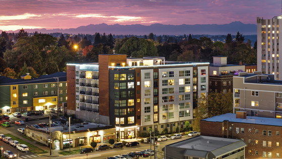 Chic urban apartment building with modern design and vibrant cityscape backdrop, beautifully illuminated during sunset.