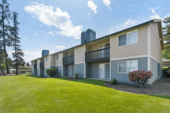 Bright and inviting two-story apartment exterior with spacious balconies, surrounded by lush green lawn and vibrant landscaping.