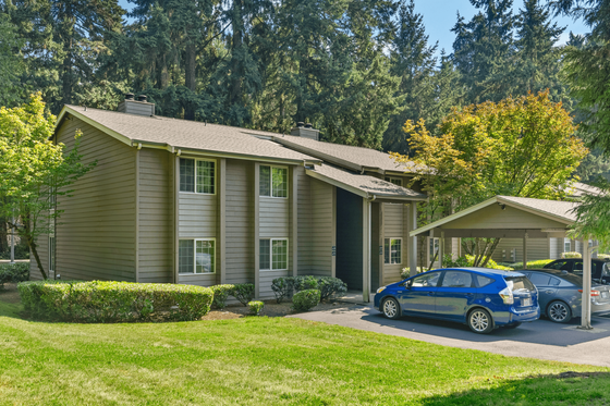 Charming suburban apartment building nestled in lush greenery with covered parking spaces and modern design.