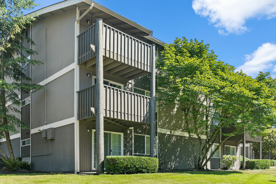 Charming multi-story apartment building with private balconies, surrounded by lush greenery on a sunny day.