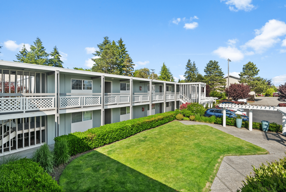 Charming apartment building with manicured landscaping, spacious balconies, and ample parking under a clear blue sky.