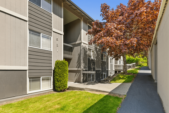Charming modern apartment exterior with lush green landscaping and vibrant trees, featuring natural wood siding and large windows.